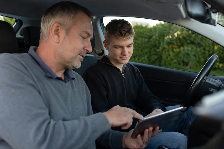 Fahrlehrer und Fahrschüler prüfen nach einer Abendfahrt eine Fahrstundenübersicht